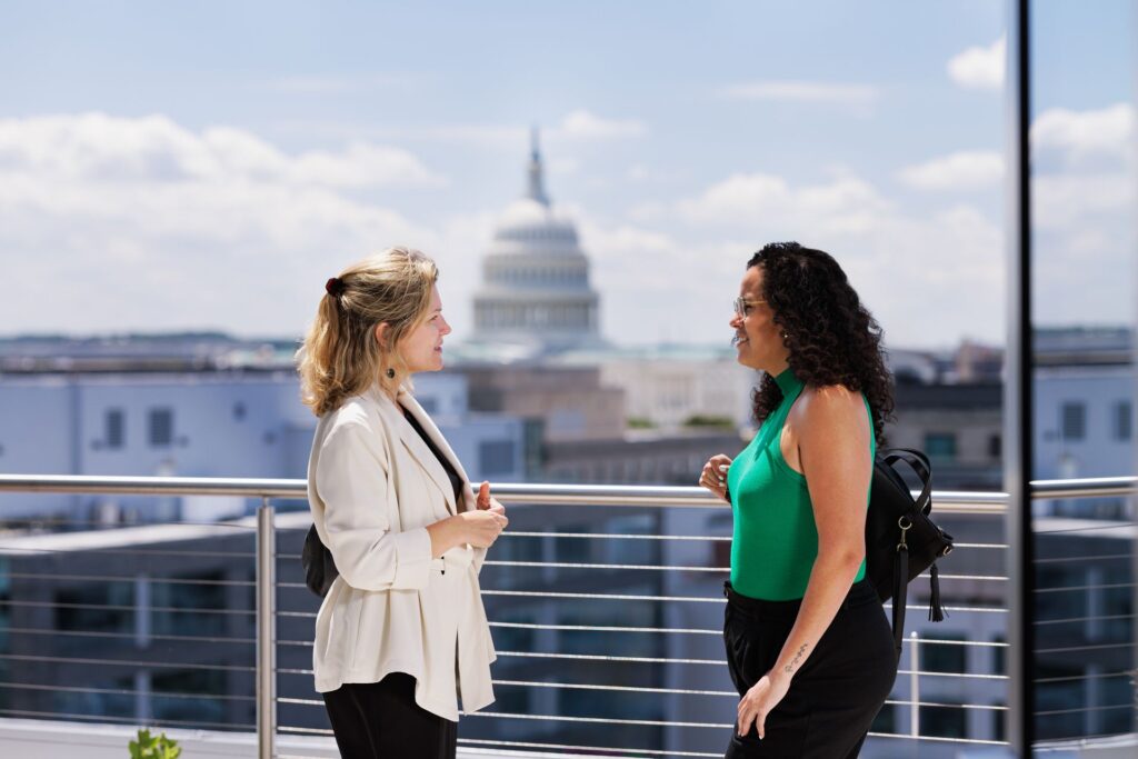 Two students talking on the roof of the new Capitol Campus building with the Capitol Building in the distance.